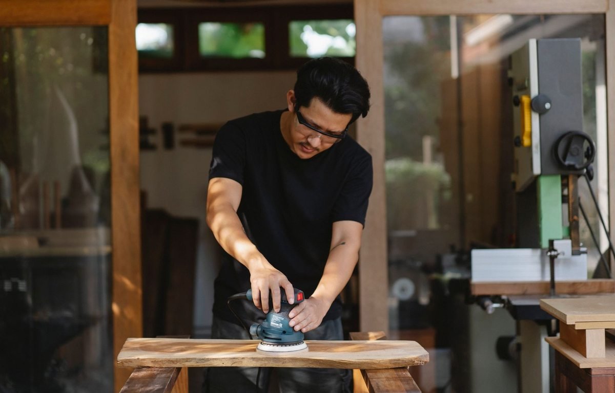 Homme ponçant du bois dans un atelier, outils et machines à proximité